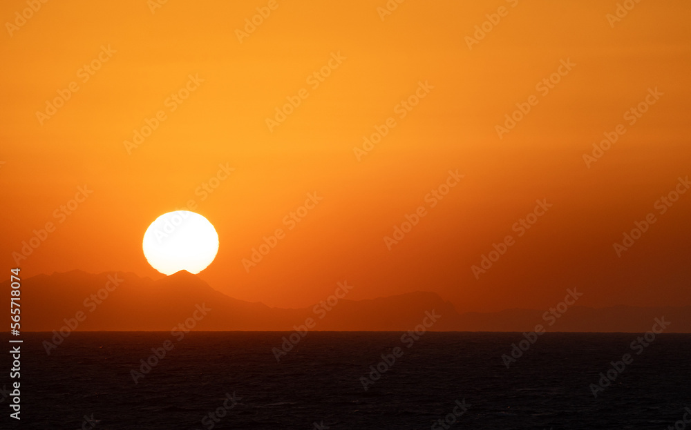 The Sun Falling Behind Mountain peak with sea foreground. A Spectacular golden Sunset 