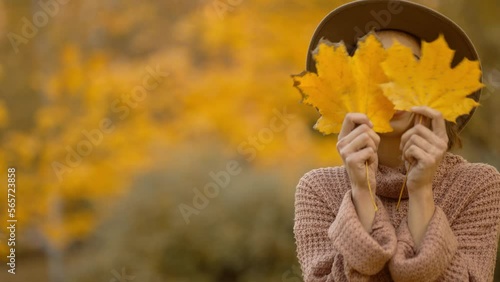 autumn portrait of beautiful smiling woman wearing in wrown dress, sweater and hat. girl holds yellow leaves and playfuly looking at camera photo