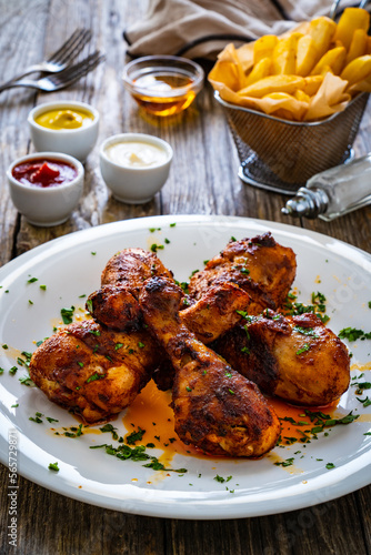 Barbecue chicken drumsticks with French fries on wooden table 