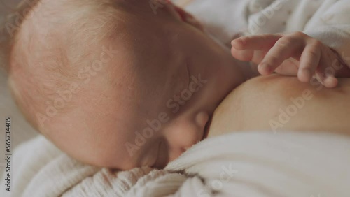 Close-up view from above of a young mother holding her baby boy closer to the chest and breastfeeding in slow-motion