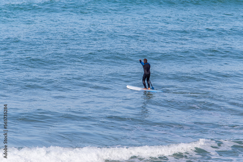 Longboards are very stable boards that are easy to lay on, sit on, paddle on, hit the waves and ride on. They with round nose and tale. In distance A man with a paddle he Longboards are very stable boards that are easy to lay on, sit on, paddle on, hit the waves and ride on. They with round nose and tale. In distance A man with a paddle he