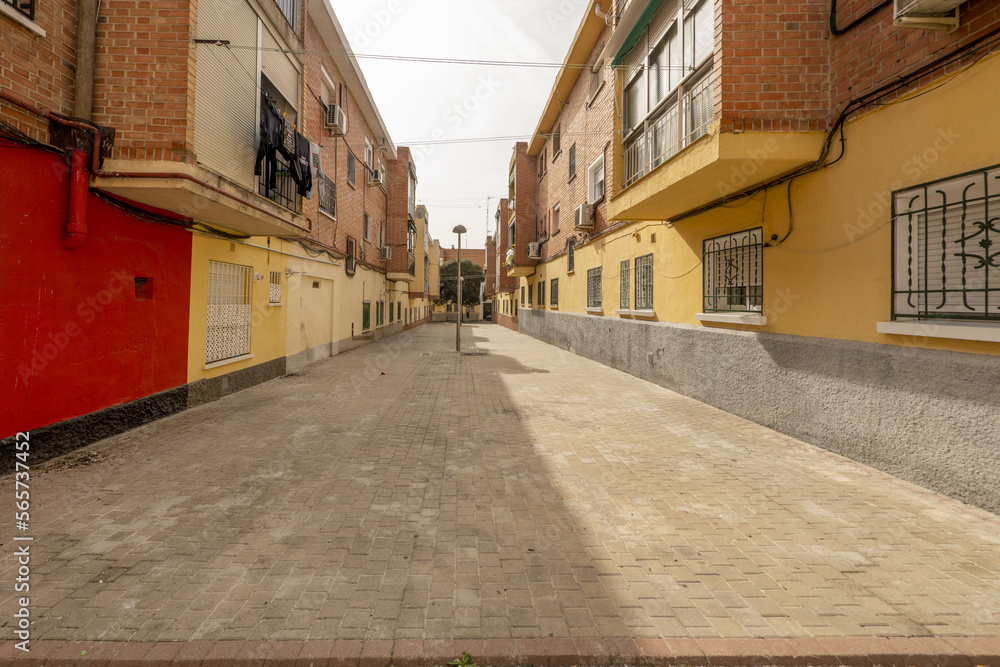 Pedestrian street between buildings with brick facades and metal gates on the ground floors