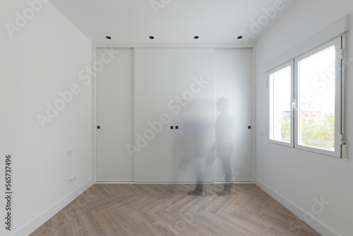 Built-in wardrobe with white wooden sliding doors in a room with aluminum windows and a ghost passing in front of the wardrobe