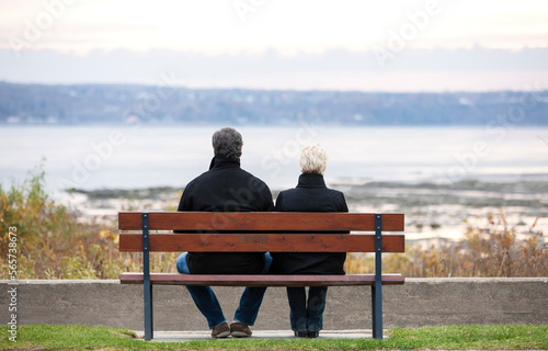 Rear view of mature couple sitting on bench overlooking river in Autumn.