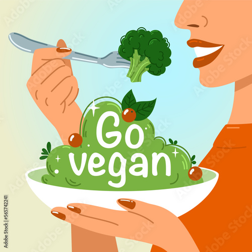  A woman holds a fork of broccoli in one hand and a plate with the inscription go vegan in the other hand