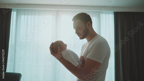 Young bearded father holding his newborn baby in arms, looking and smiling at the baby in slow-motion photo