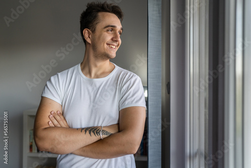 Portrait of one young adult caucasian man stand by the window at home