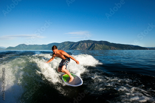 A happy man smiles while wakesurfing behind a wakeboard boat on a sunny day in Idaho. photo