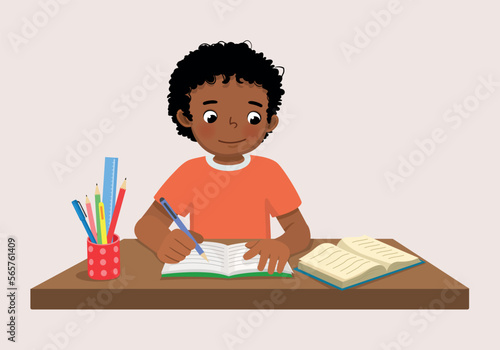 Cute little African boy sitting on the desk studying writing on notebook doing his homework at home
