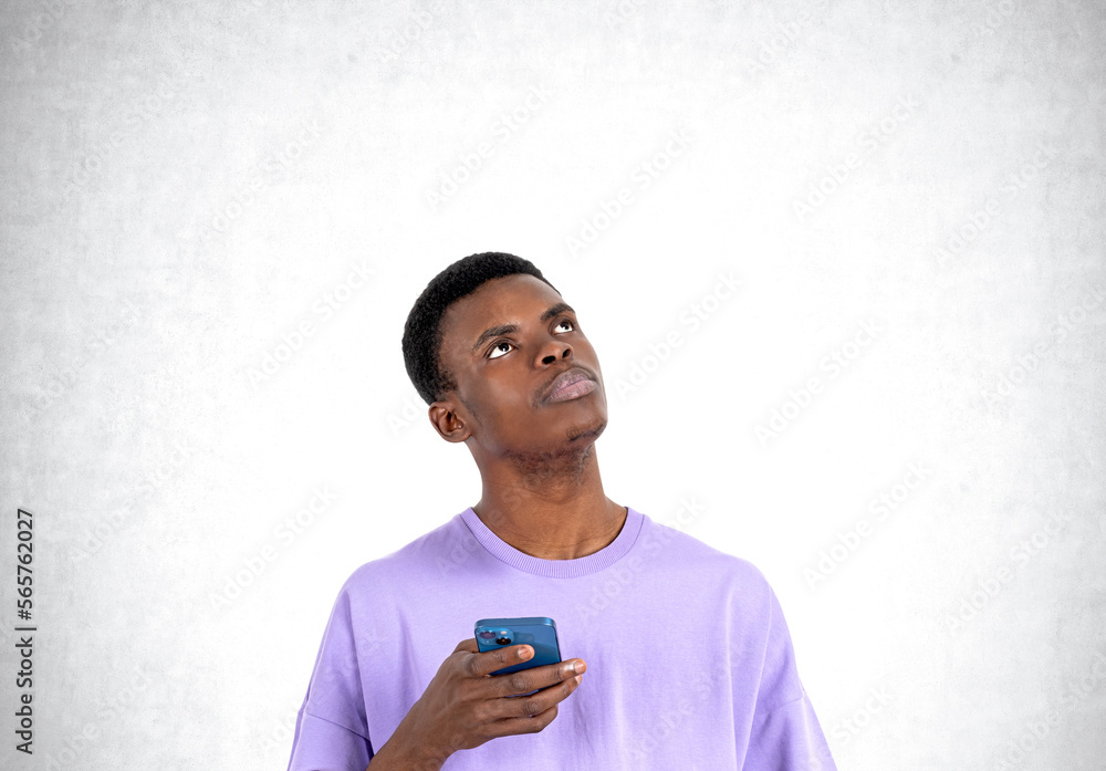 Young black man with phone and pensive look, copy space concrete wall Young black man with phone and pensive look, copy space concrete wall
