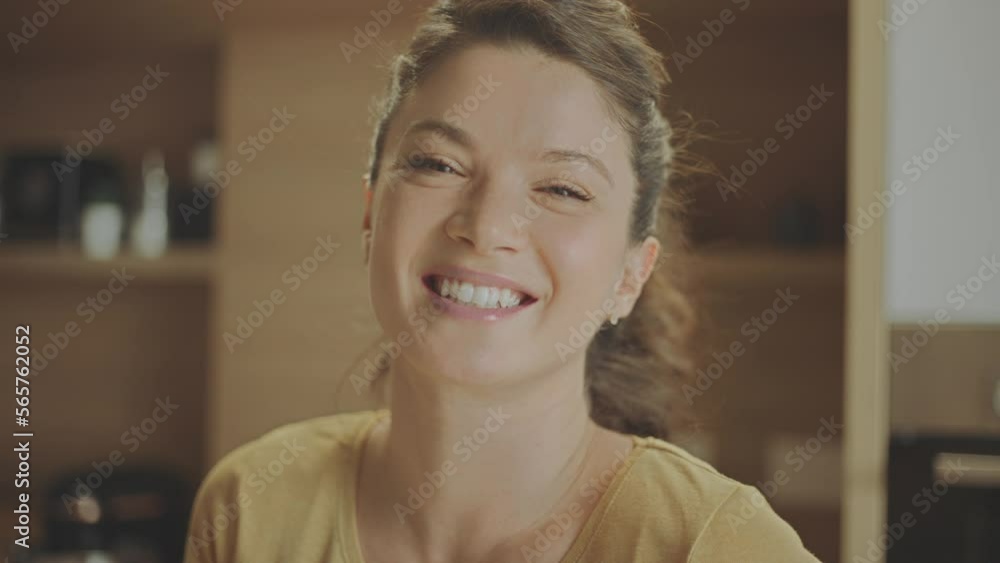 Portrait shot of a beautiful woman standing alone in the kitchen and smiling while looking at camera in slow-motion Portrait shot of a beautiful woman standing alone in the kitchen and smiling while looking at camera in slow-motion
