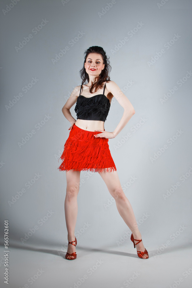 An elegant dancer performs a Latin American dance in an elegant red dress with sparkling jewelry. Fashion and beauty. Ballet show. Studio portrait. An elegant dancer performs a Latin American dance in an elegant red dress with sparkling jewelry. Fashion and beauty. Ballet show. Studio portrait.