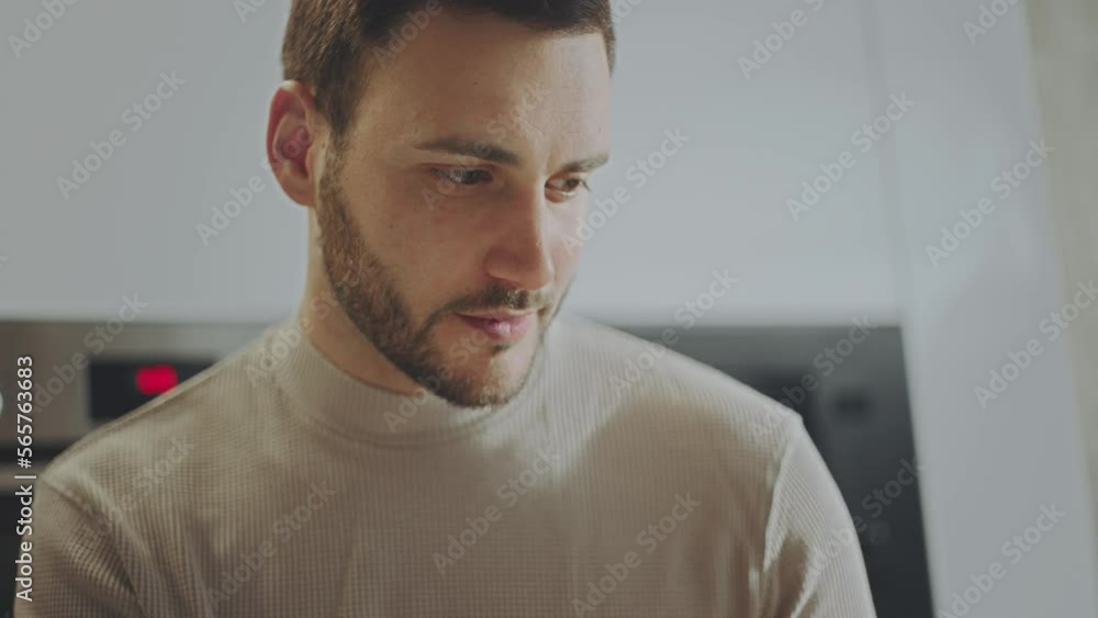 Close-up view of a handsome man sitting on the desk at home, looking at laptop and working remotely Close-up view of a handsome man sitting on the desk at home, looking at laptop and working remotely