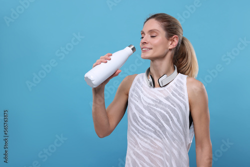 Sportswoman with thermo bottle and headphones on light blue background, space for text © New Africa