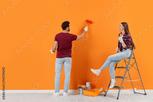 Картината върху платно Man painting orange wall and woman sitting on folding ladder indoors