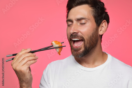 Handsome man eating tasty sushi with chopsticks on pink background