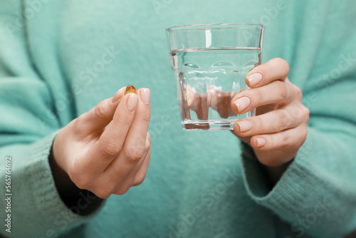 Woman holding glass of water and pill, closeup view