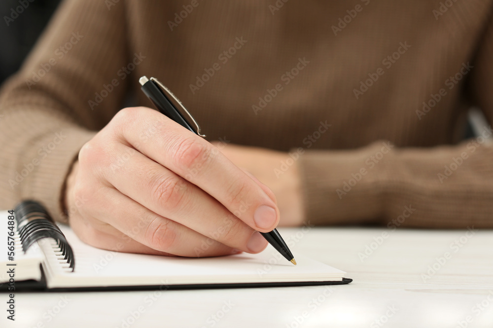 Man writing in notebook at white table, closeup. Space for text Man writing in notebook at white table, closeup. Space for text