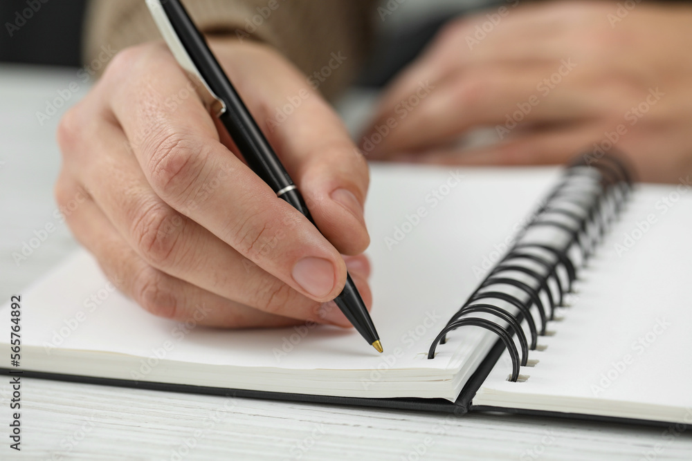 Man writing in notebook at white wooden table, closeup Man writing in notebook at white wooden table, closeup