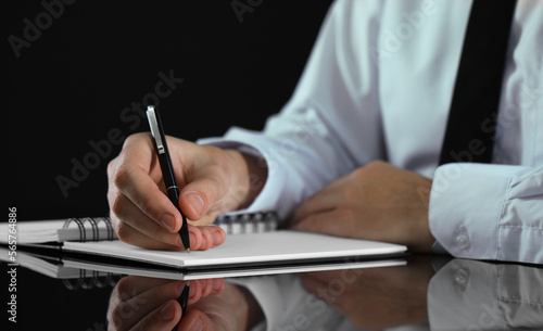 Man writing in notebook at black table, closeup