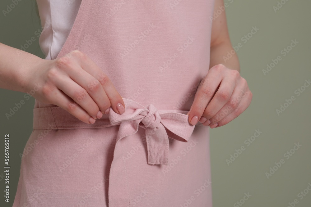 Woman putting on pink apron against light green background, closeup Woman putting on pink apron against light green background, closeup