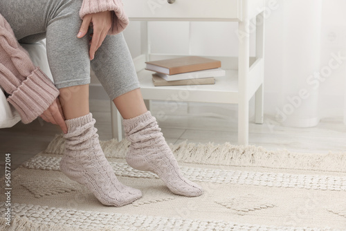 Woman wearing warm knitted socks at home, closeup. Space for text photo