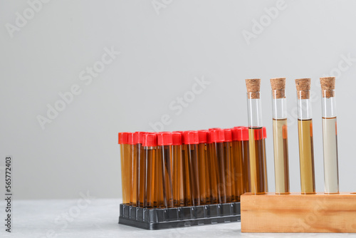 Test tubes with brown liquids in stands on white table against light background. Space for text