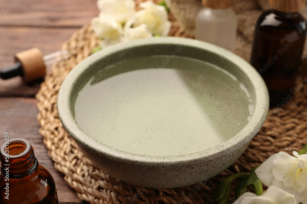 Bowl of essential oil and beautiful flowers on wooden table, closeup. Aromatherapy treatment Bowl of essential oil and beautiful flowers on wooden table, closeup. Aromatherapy treatment