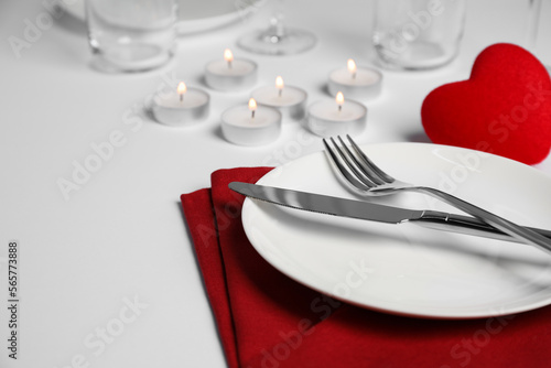 Beautiful table setting with burning candles on white table, closeup. Romantic dinner. Space for text