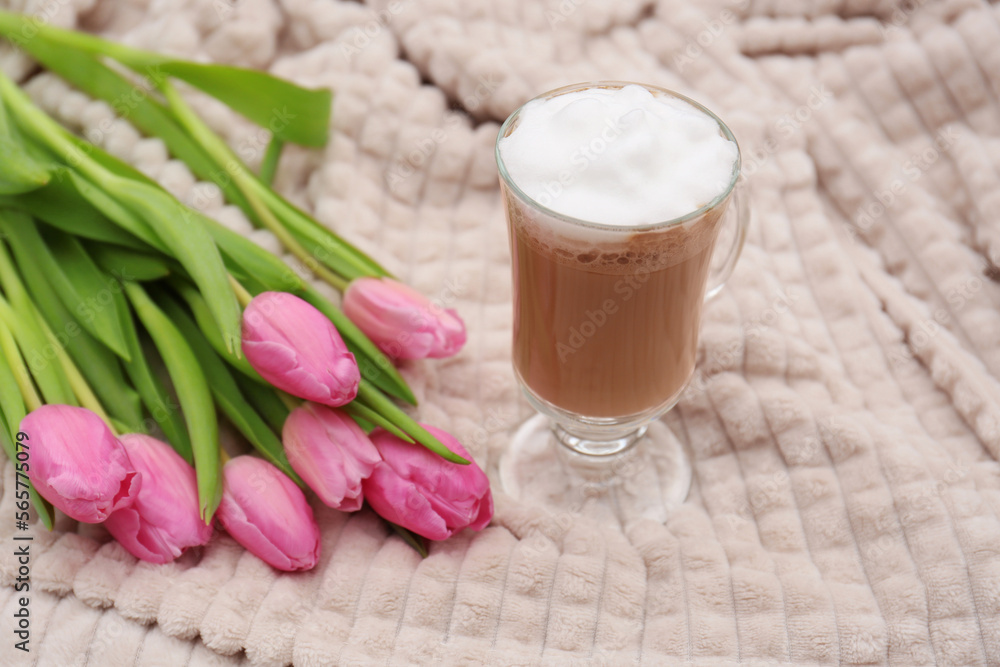Glass of delicious cocoa and pink tulips on light blanket