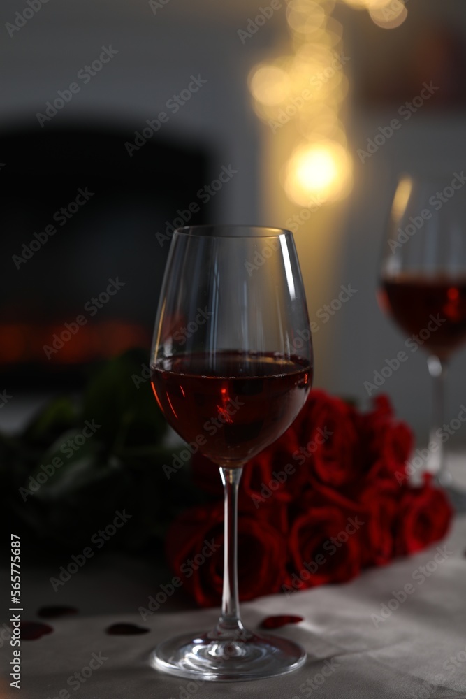 Glasses of red wine and rose flowers on grey table against blurred lights. Romantic atmosphere
