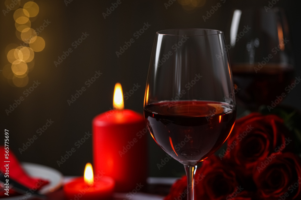 Glasses of red wine, burning candles and rose flowers against blurred lights, space for text. Romantic atmosphere Glasses of red wine, burning candles and rose flowers against blurred lights, space for text. Romantic atmosphere
