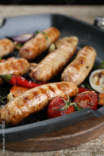Tasty fresh grilled sausages with vegetables on wooden table, closeup