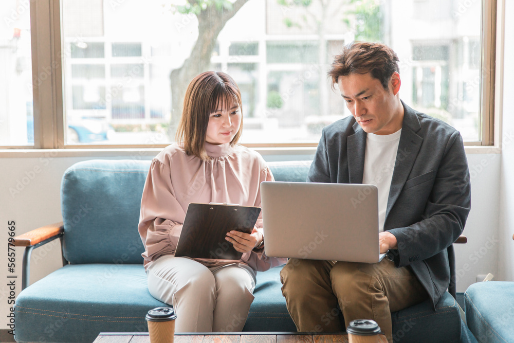 Fototapeta premium カフェでパソコンを使って仕事を教える・話すビジネスマンとビジネスウーマン(アジア人・男女)