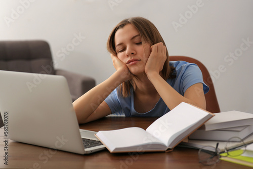 Young tired woman sleeping near books at wooden table indoors © New Africa