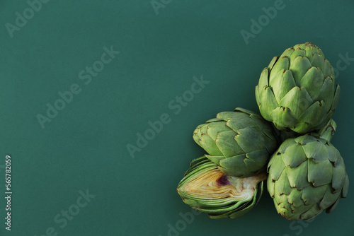 Cut and whole fresh raw artichokes on green background, flat lay. Space for text