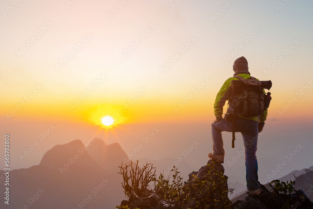 Male Hiker with backpack relaxing on top of rock mountain and enjoying sunset sky.