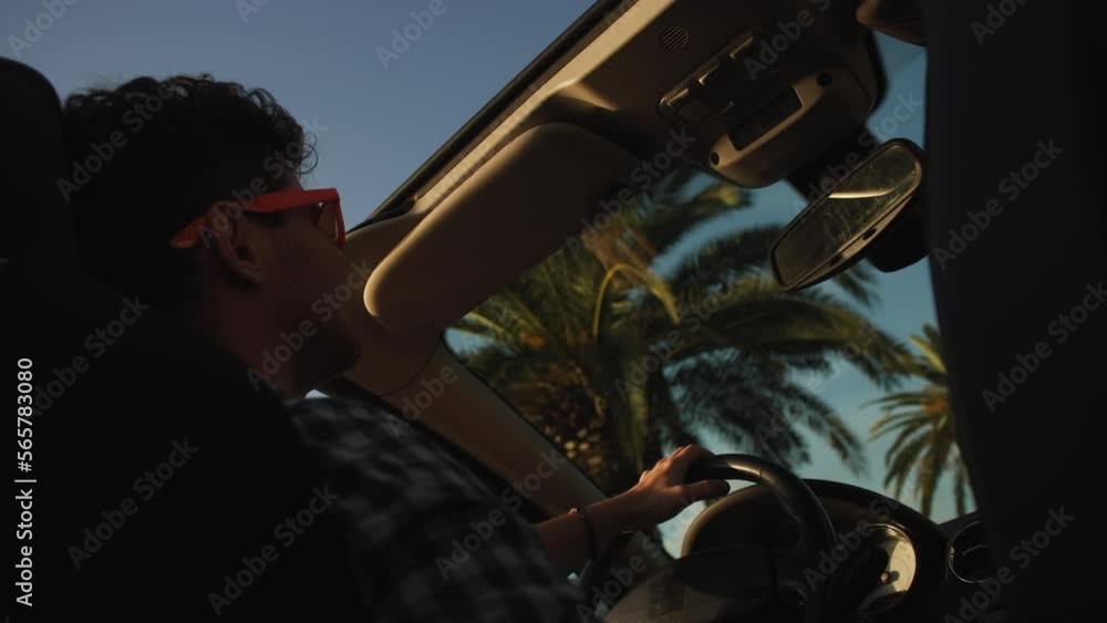 Man raises their hands in delight in the air against the background of palm trees and sunset on the seashore Man raises their hands in delight in the air against the background of palm trees and sunset on the seashore
