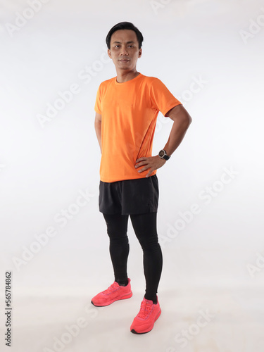 Strong confidence athletic young Asian male wearing running jersey looking at camera with hands on hips, full length studio shot portrait against white