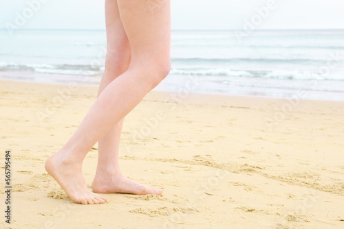 Women's feet on the beach. A bare-legged woman walks along the sand towards the sea. Barefoot woman walking on beach. Beach holiday concept.