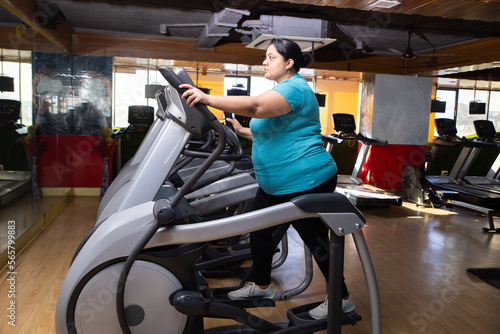 Young overweight indian woman is workout in gym to lose weight. Asian female doing cardio training on bicycle machine. Full length.