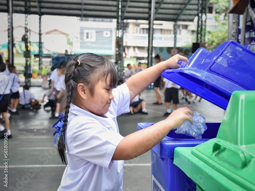 Elementary school students are throwing garbage into the bin with a smiling face.