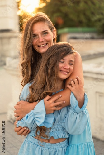 Mother daughter sunset. in blue dresses with flowing long hair against the backdrop of sunset. The woman hugs and presses the girl to her.