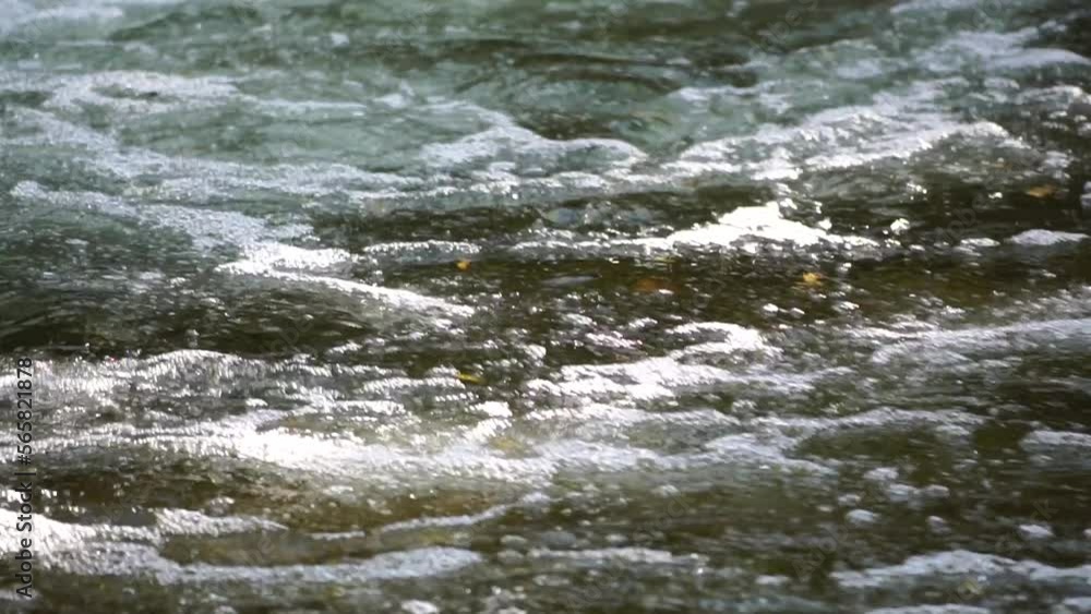 Slow motion closeup of a rushing stream, swift flow of spring water with some autumn colourful leaves in the water. Grey big stones, fallen autumnal leaves. Waterfall at fall. Nature's landscape. Slow motion closeup of a rushing stream, swift flow of spring water with some autumn colourful leaves in the water. Grey big stones, fallen autumnal leaves. Waterfall at fall. Nature's landscape.