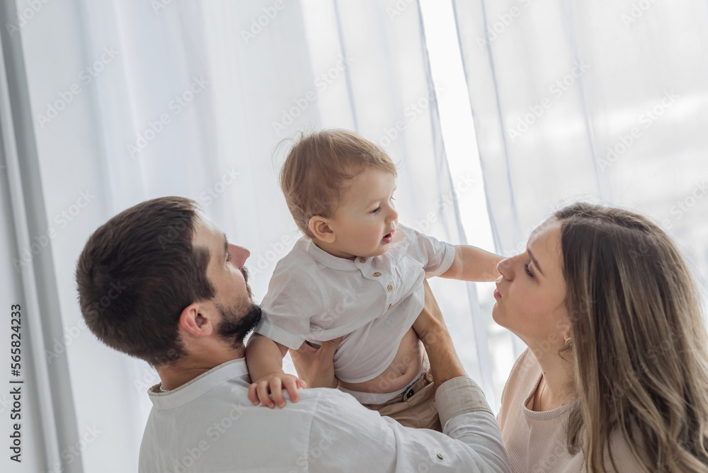 Happy cheerful parents having fun with cute child son cuddling playing near window. Happy cheerful parents having fun with cute child son cuddling playing near window.