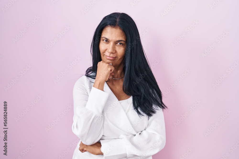 Mature hispanic woman standing over pink background with hand on chin thinking about question, pensive expression. smiling and thoughtful face. doubt concept. Mature hispanic woman standing over pink background with hand on chin thinking about question, pensive expression. smiling and thoughtful face. doubt concept.