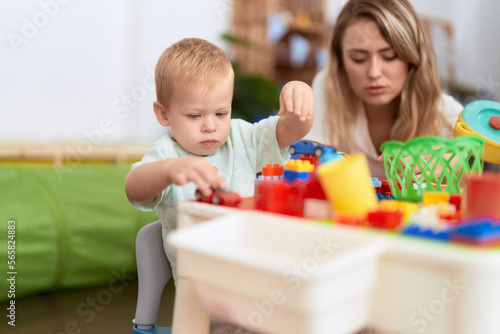 Teacher and toddler playing with construction blocks and car toy sitting on table at kindergarten