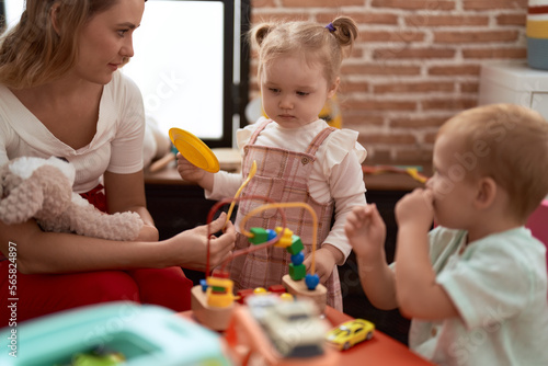 Teacher with boy and girl playing with toys sitting on table at kindergarten