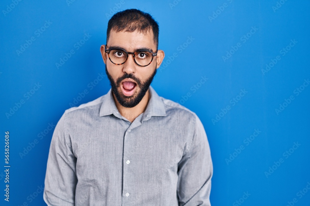 Obraz premium Middle east man with beard standing over blue background afraid and shocked with surprise expression, fear and excited face.