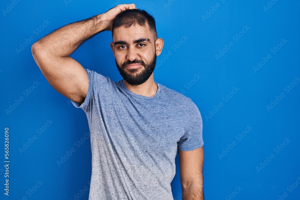 Middle east man with beard standing over blue background confuse and wondering about question. uncertain with doubt, thinking with hand on head. pensive concept. Middle east man with beard standing over blue background confuse and wondering about question. uncertain with doubt, thinking with hand on head. pensive concept.